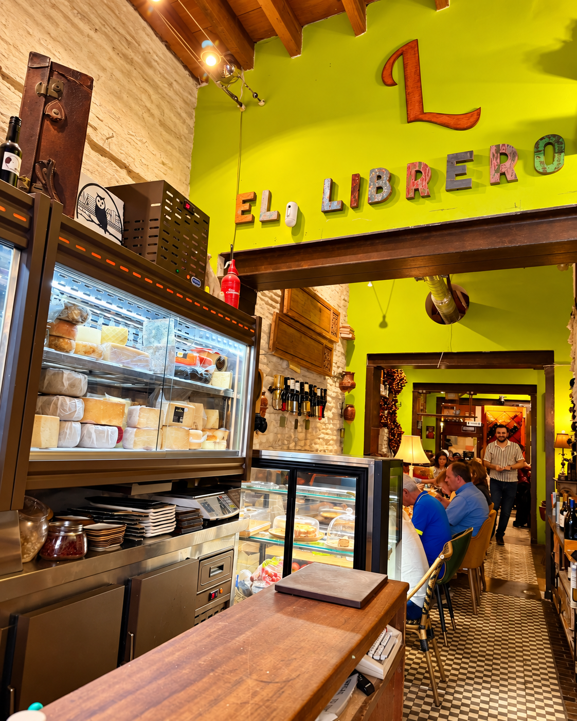 Interior de El Librero con pared verde y vitrina de quesos
